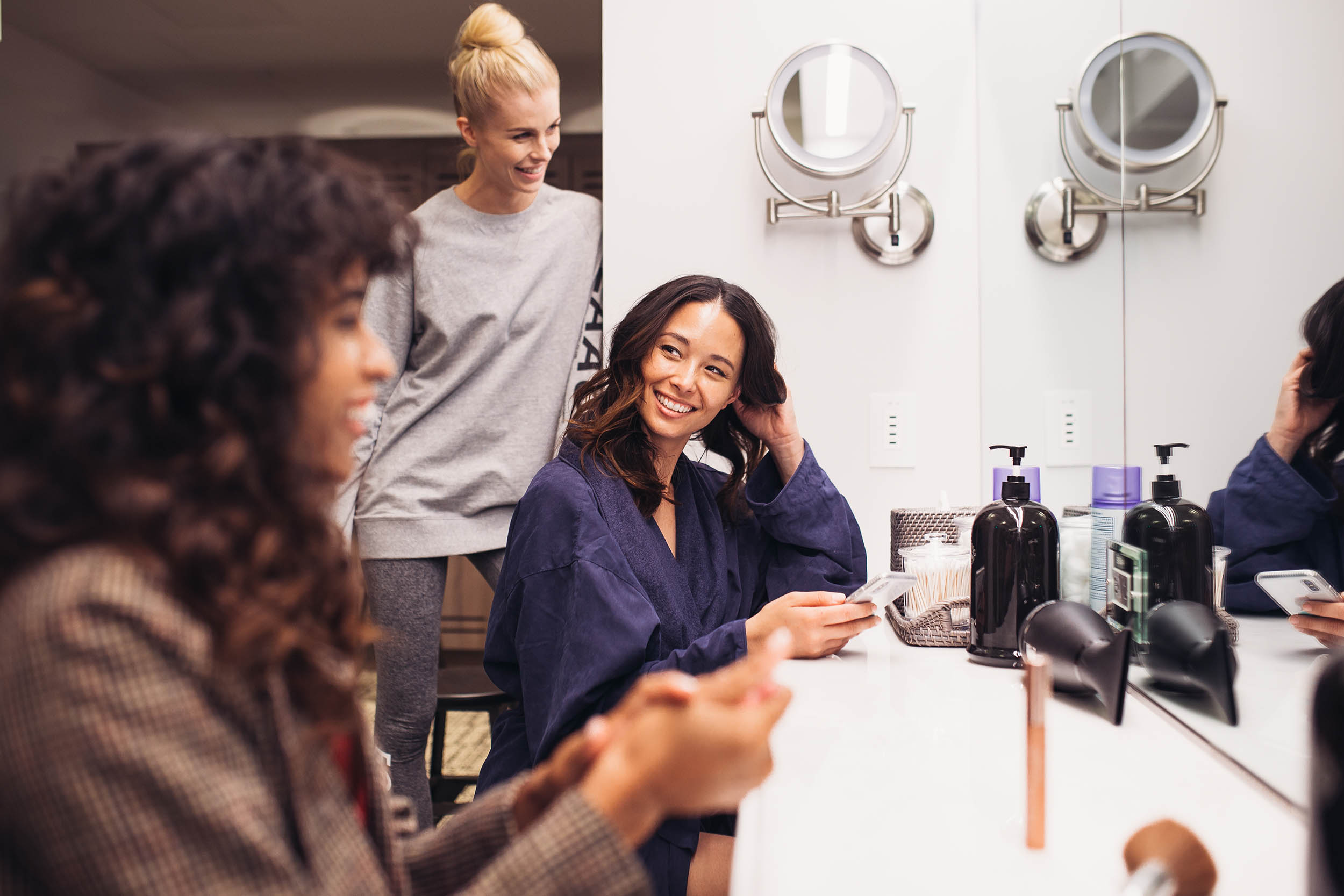 Two women at Los Angeles Athletic Club salon in front of a mirror, one woman looking at her phone.