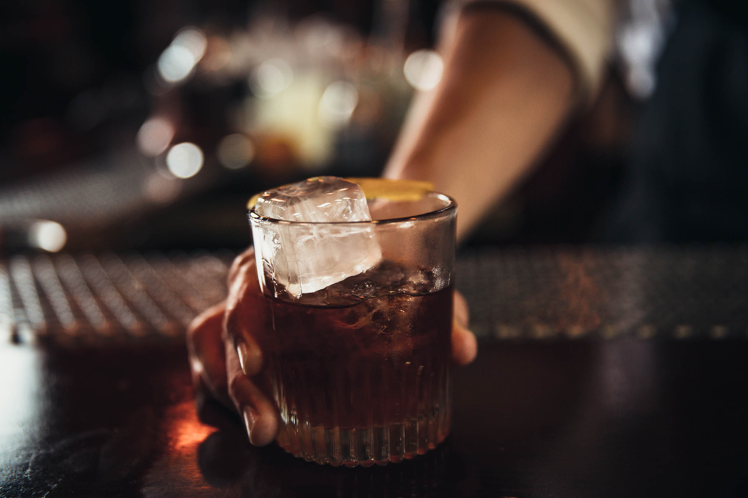 A bartender holding a glass of alcohol, ready to serve a customer at a bar counter.